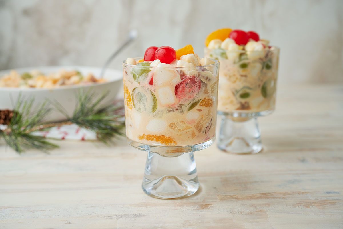 Close-up shot of the Christmas Fruit Salad, highlighting the bright colors of maraschino cherries, mandarin oranges, and grapes mixed with whipped cream and marshmallows.