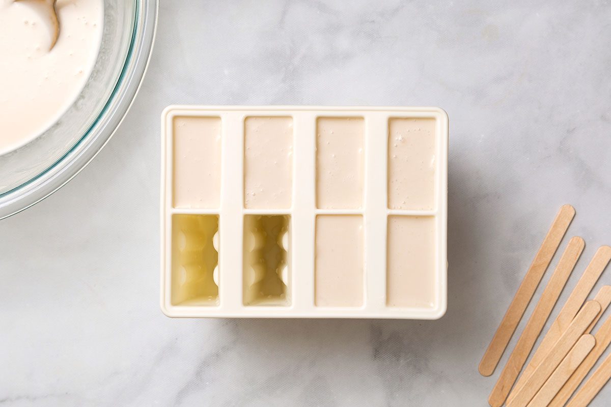 Coconut popsicle liquid mixture in popsicle molds for step two of Coconut Popsicles for Taste of Home