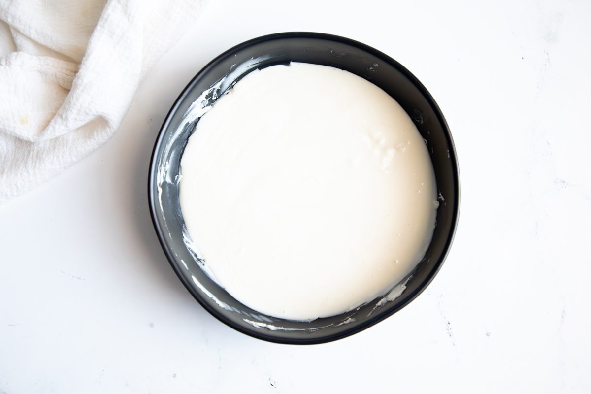 Overhead shot for Taste of Home Coconut Snowballs, melted white chocolate and shortening in a black bowl.