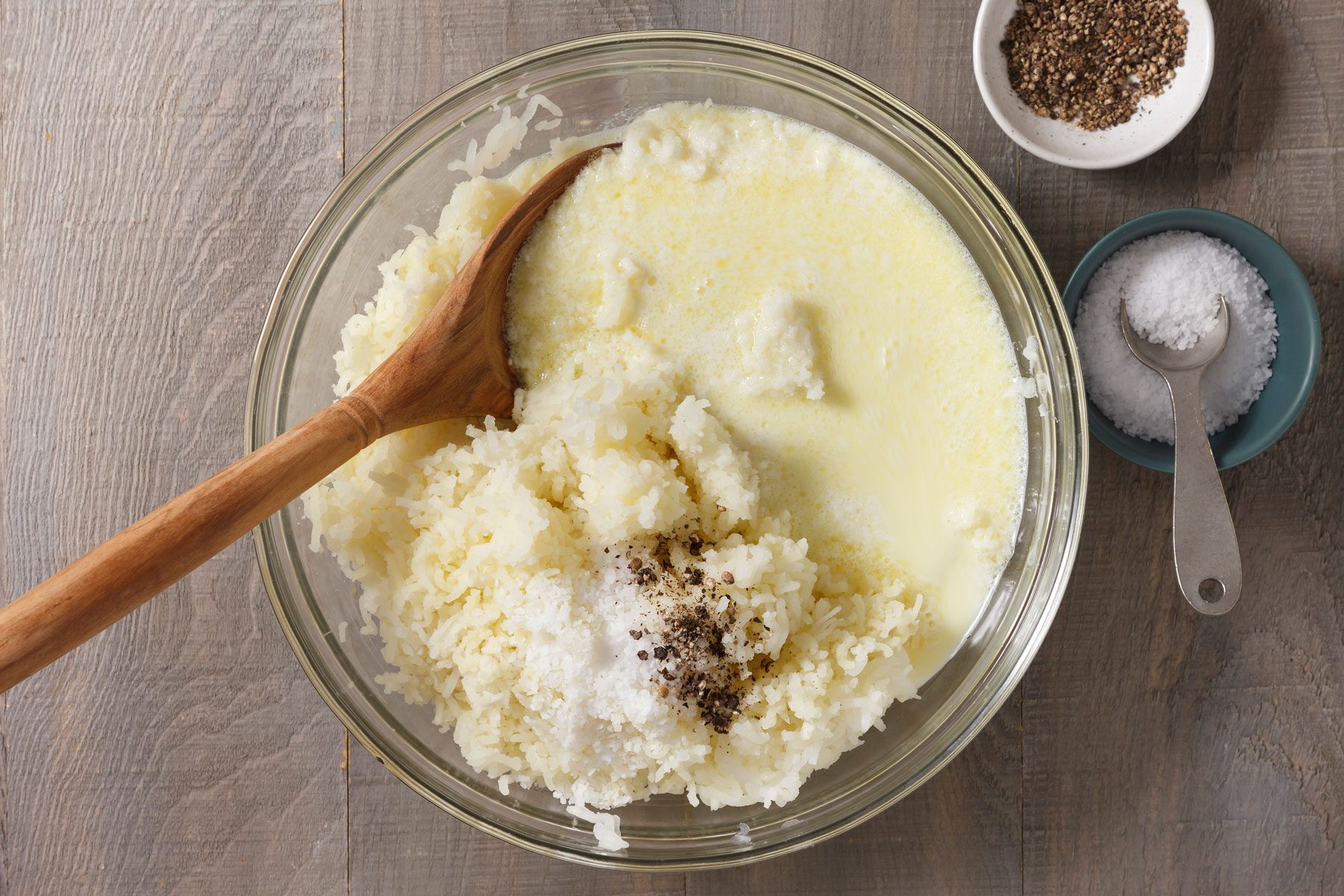 Milk, cream and butter mixture added to mashed potatoes in a large bowl.