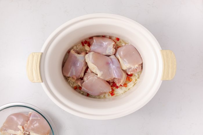 Chicken thighs layered on top of veggies in slow cooker.
