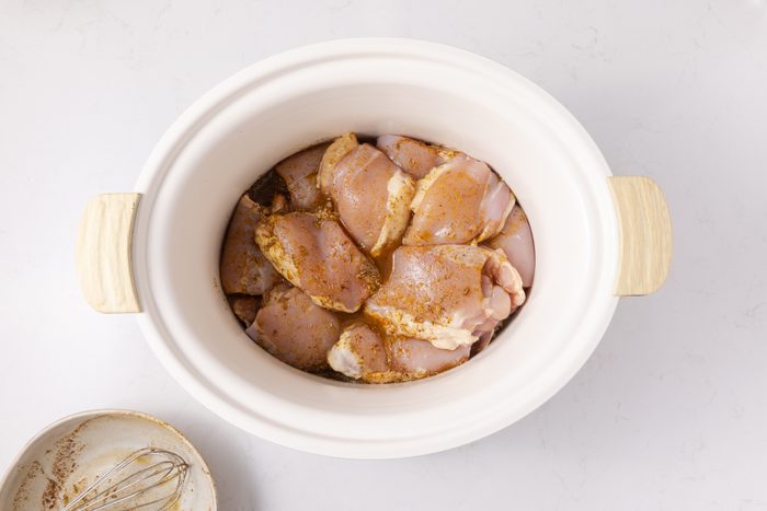 Chicken thighs in slow cooker topped with seasoned broth.