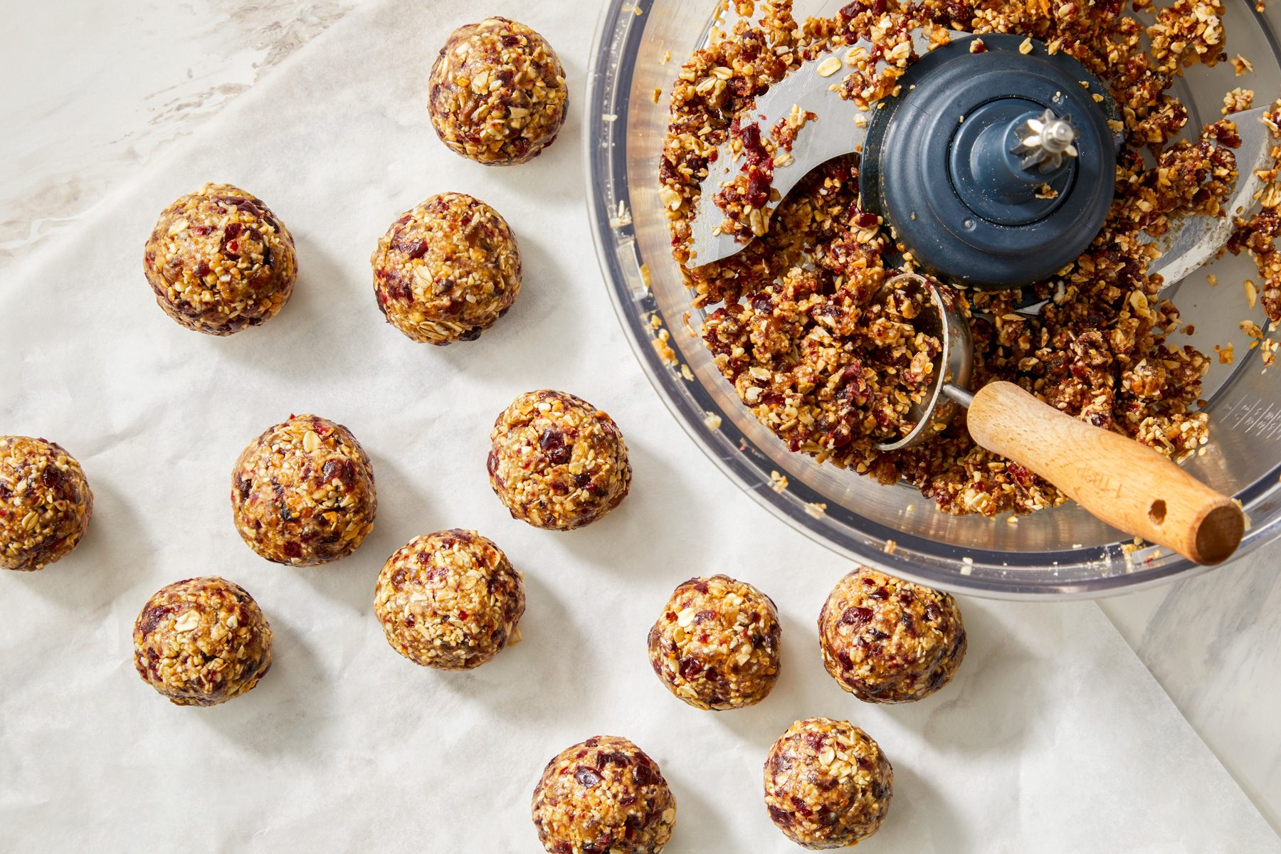 Shaping a sticky mixture into 1.5-inch balls, with several finished energy balls resting on a parchment-line. 