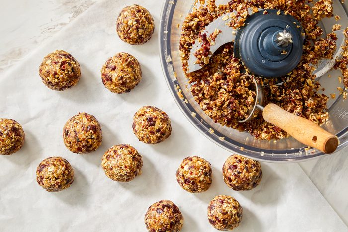 Shaping a sticky mixture into 1.5-inch balls, with several finished energy balls resting on a parchment-line.