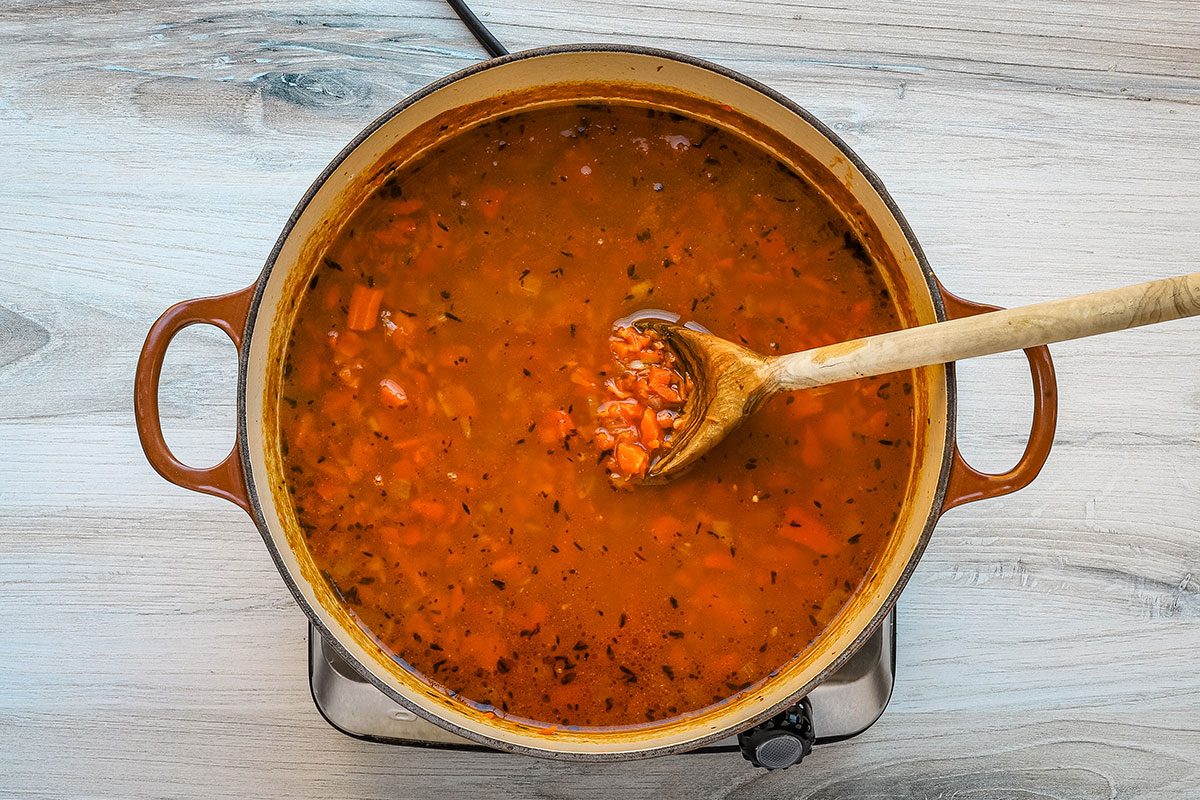 Carrot soup preparation in a Dutch oven with chopped carrots, seasonings, onions, garlic and vegetable broth.