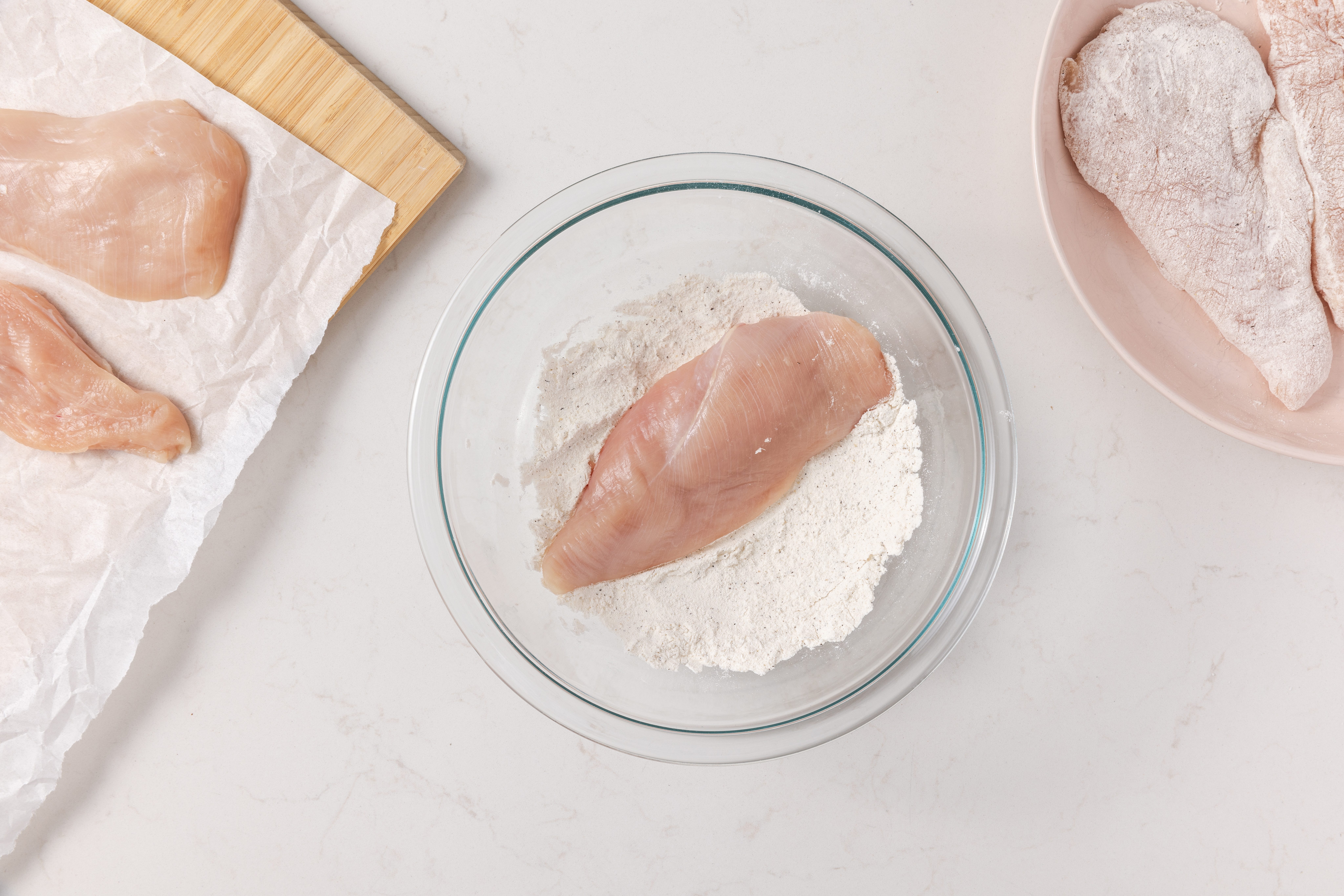 Chicken breast being coated with flour in shalow bowl.