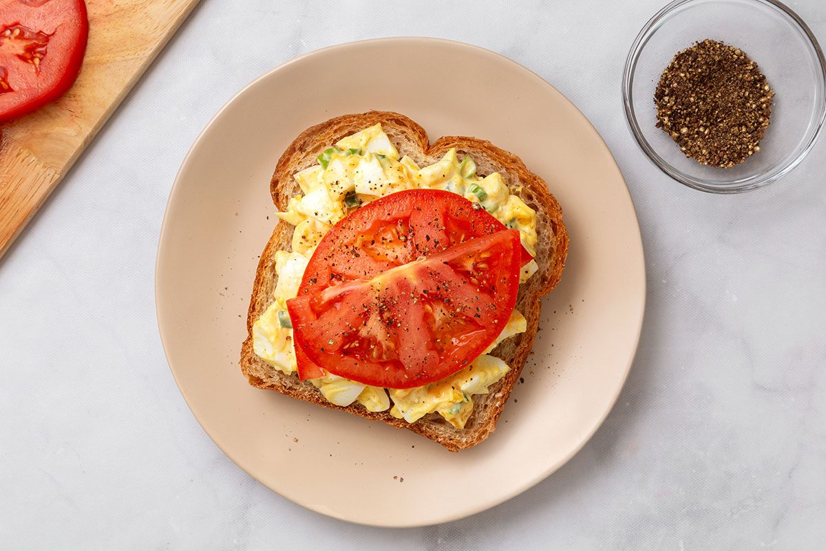 Whole wheat bread slices topped with curried egg salad and seasoned tomato slices for step three of Curried Egg Salad recipe for Taste of Home