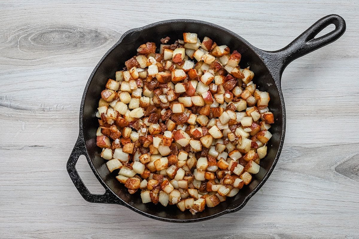 Cooked potatoes in a cast iron skillet for a meal of potatoes and eggs.