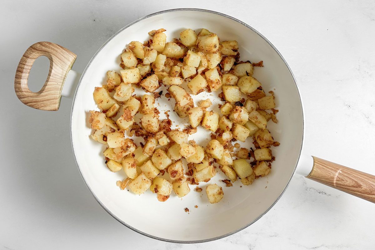 Potatoes and onions for Taste of Home Farmers Breakfast in a white skillet