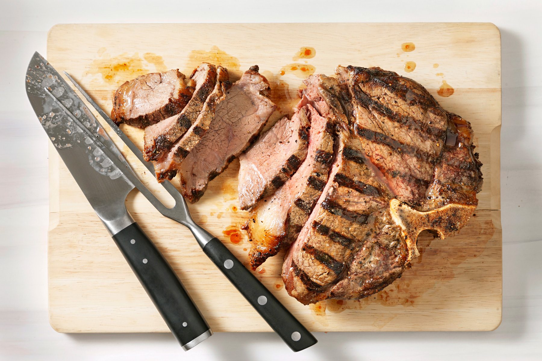 The grilled steak is being sliced on a chopping board, showcasing its juicy interior and perfectly cooked exterior.