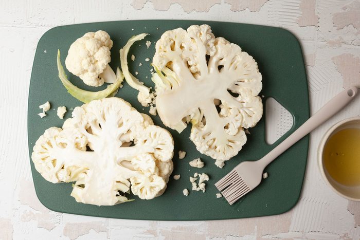 Step 1 of Taste of Home Grilled Cauliflower Steaks is to cut through the core of the cauliflower into four 1 inch thick steaks. Brush both sides of the cauliflower with oil.