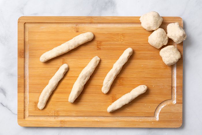 Bread dough shaped in 6-inch ropes on a wooden cutting board for step four of Homemade Breadsticks for Taste of Home