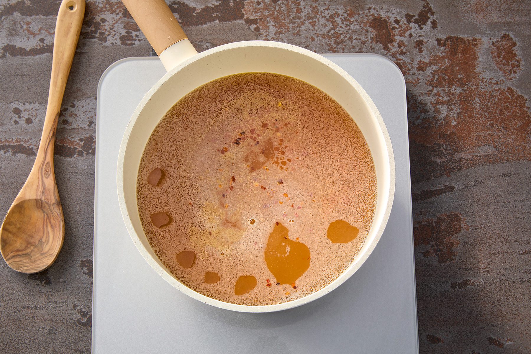 Overhead shot of stir in rice vinegar; soy sauce; chili oil; salt; pepper and red pepper flakes; wooden spoon; brown texture background;