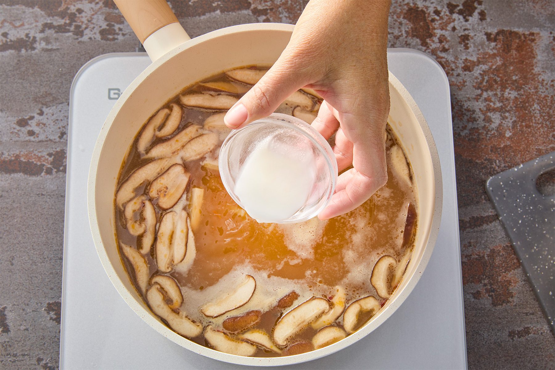 Overhead shot of a small bowl; whisk together cornstarch and water until dissolved; stir mixture into broth until thickened; 1-2 minutes; brown texture background;