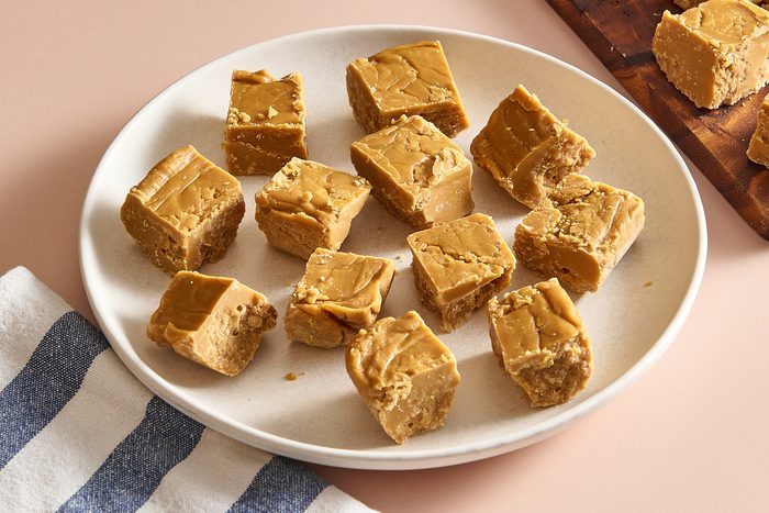 Angled shot of a plate of maple fudge with a few pieces on a cutting board in the background