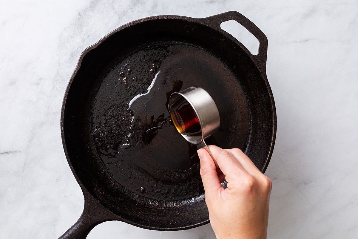 Maple syrup and vinegar in a cast iron skillet for step three of Maple-Glazed Pork Chops recipe for Taste of Home