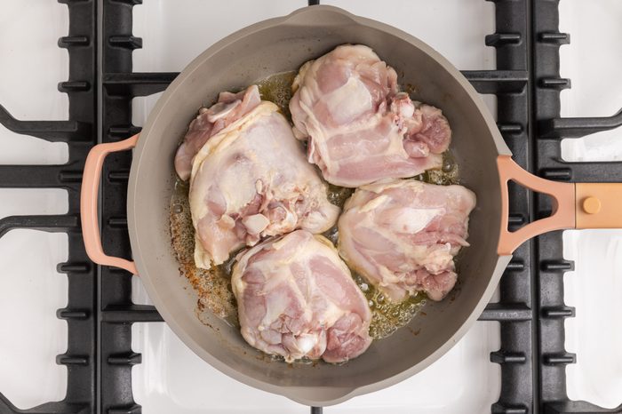 Chicken thighs being browned in large skillet.