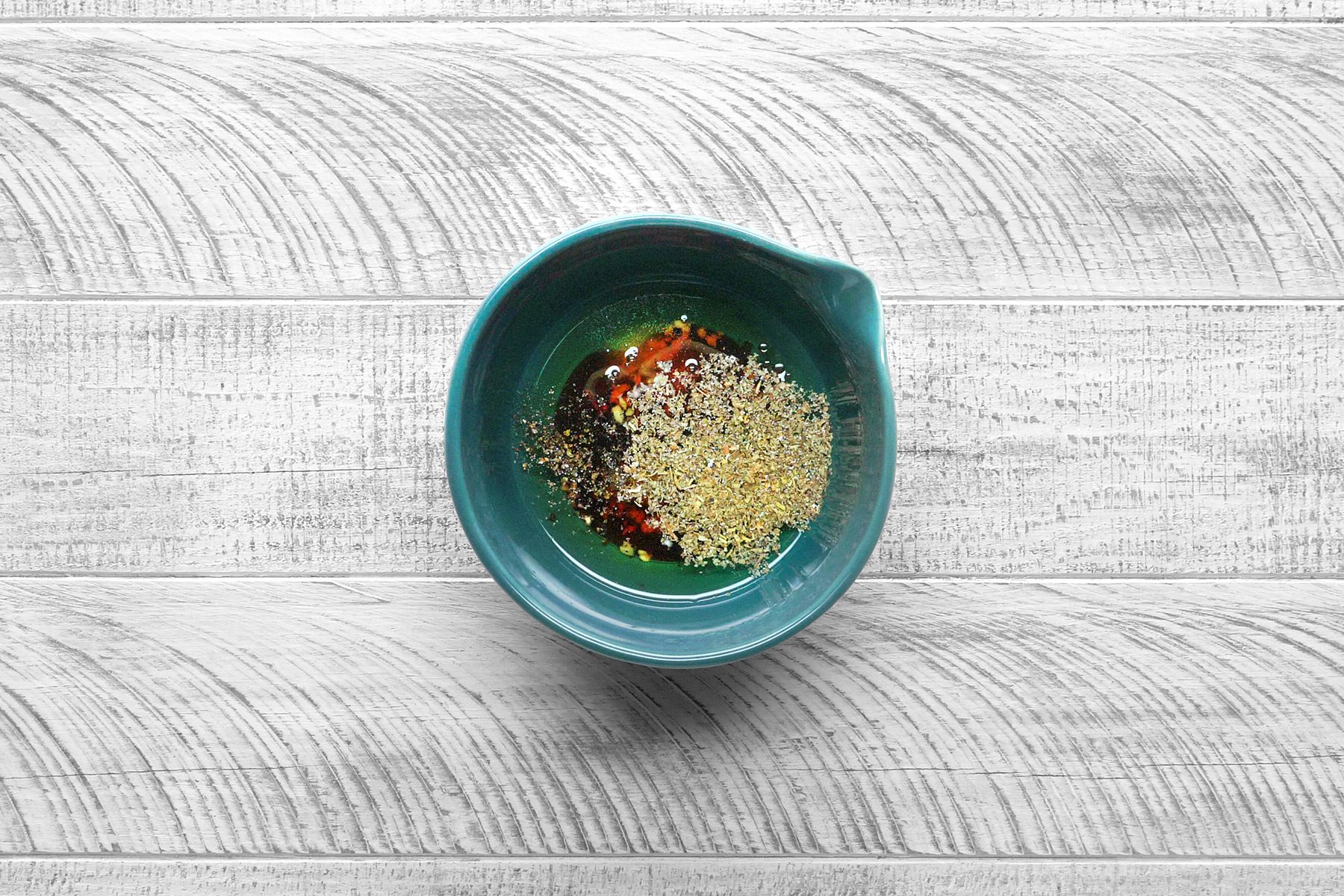 Overhead shot of a small bowl whisk the dressing ingredients; grey wooden surface