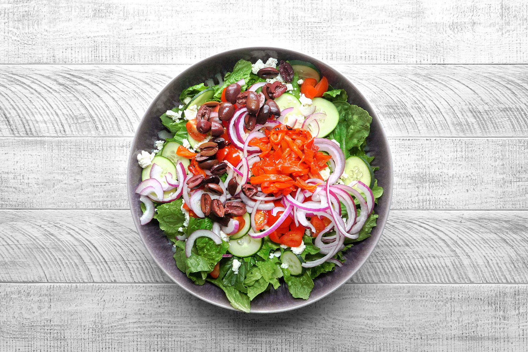 Overhead shot of a very large salad bowl combine the first 7 ingredients; grey wooden surface