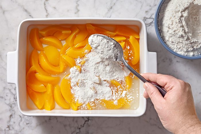 cake mix being added to peaches in a baking dish
