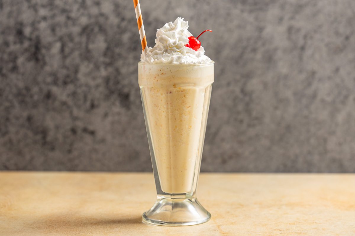 Taste of Home Peach Milkshake photo of the finished recipe topped with whipped cream and a cherry.