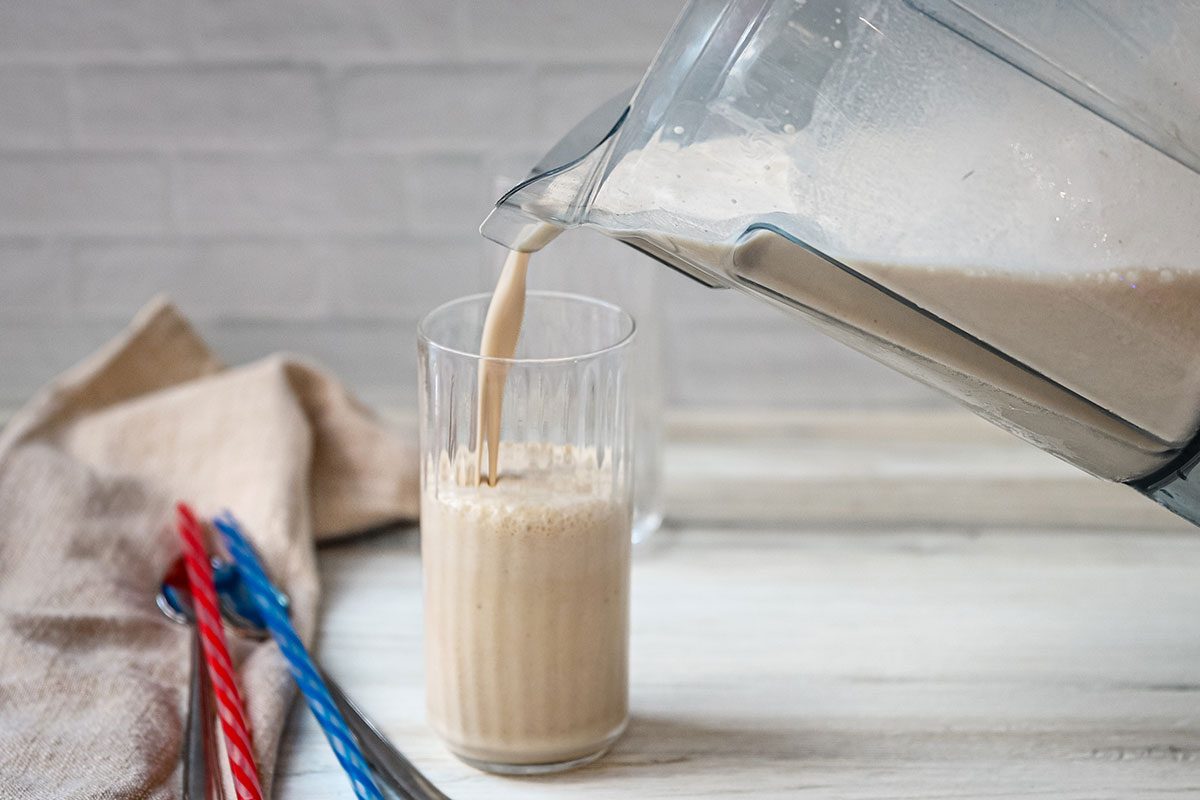 Pouring a peanut butter and banana smoothie from the blender, with straws on the side.