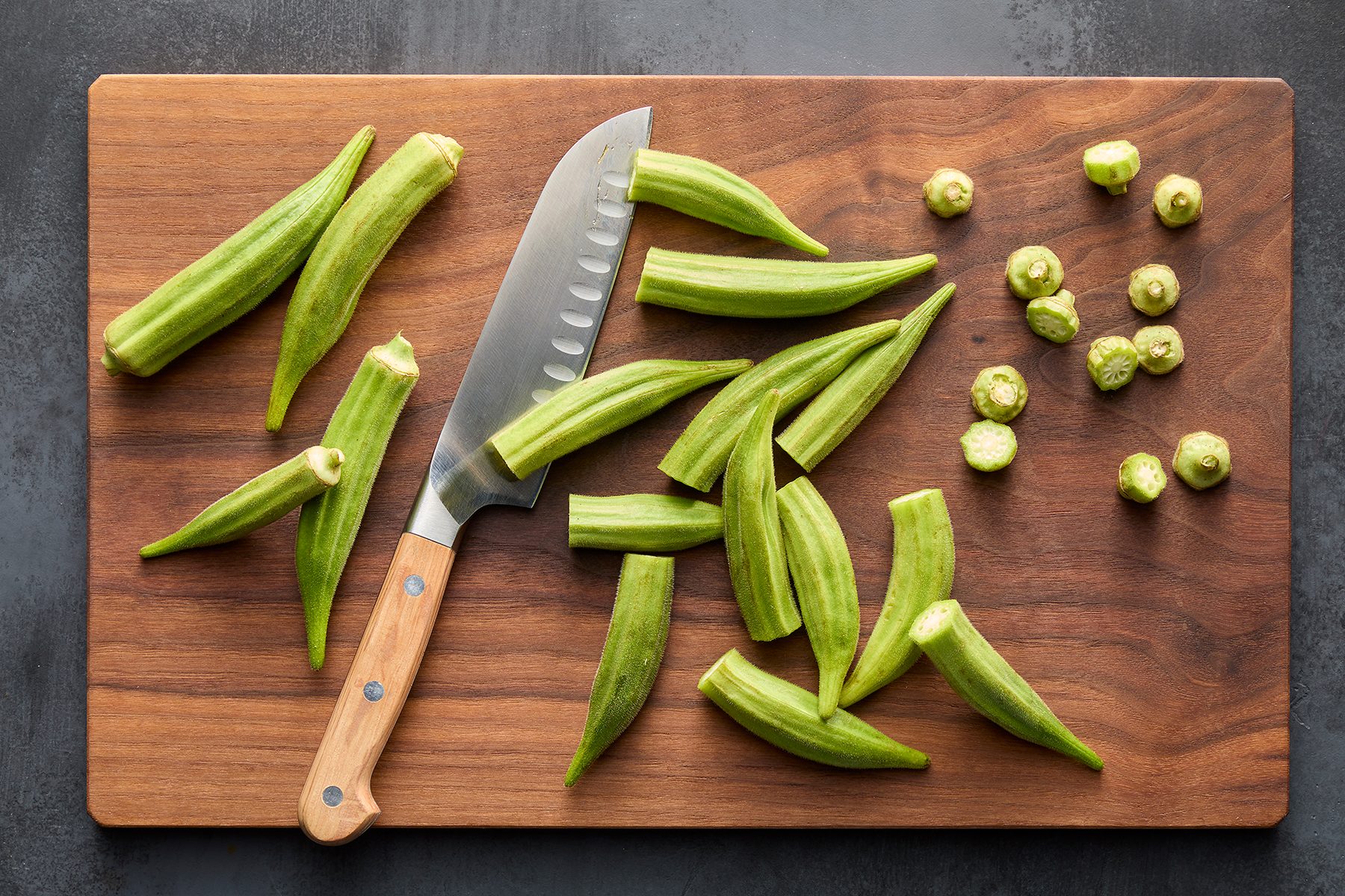 A wooden cutting board with a knife and sliced okra. Some okra pieces are whole, while others are cut.