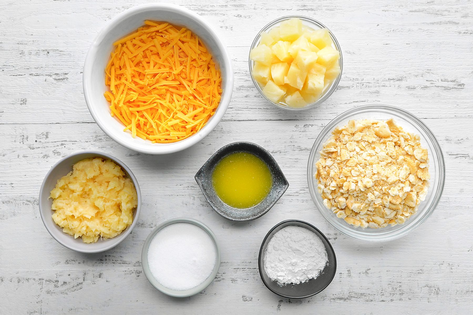 overhead shot of Pineapple Casserole ingredients placed over white wooden background;