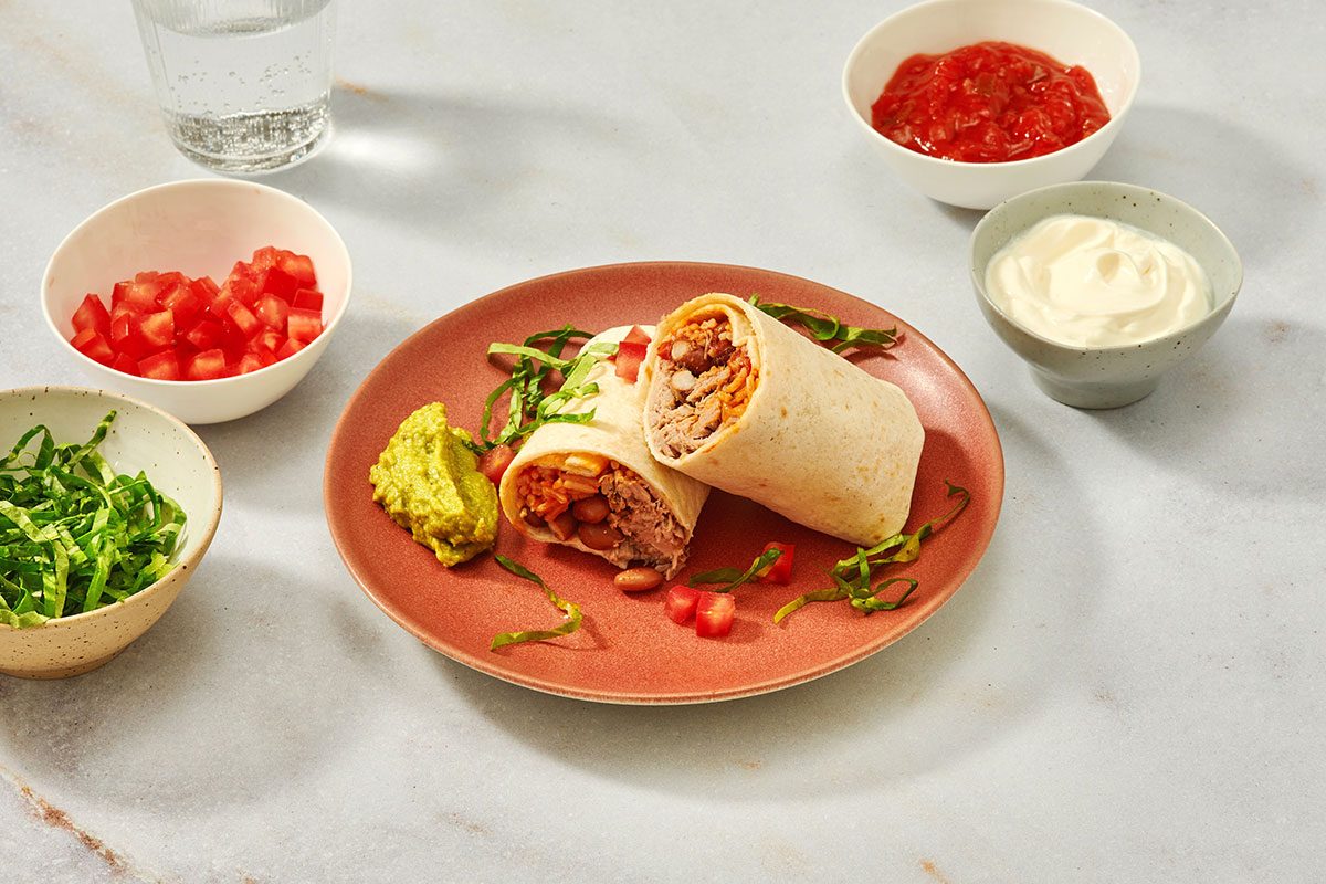 Pork burritos on a serving plate with garnishes on the side
