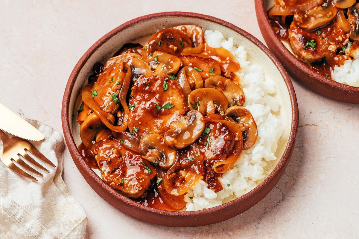 Two plates on a marble platter showing Pork Tenderloin with Gravy recipe by Taste of Home, served with hot cooked rice and a glass of wine