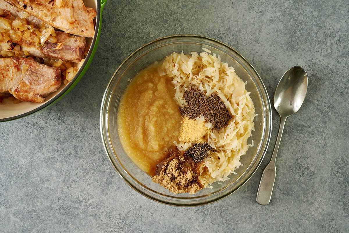 Overhead view of the sauerkraut, applesauce, brown sugar, caraway seeds, garlic powder, and pepper mixture being combined in a bowl for the Taste of Home Pork and Sauerkraut recipe.