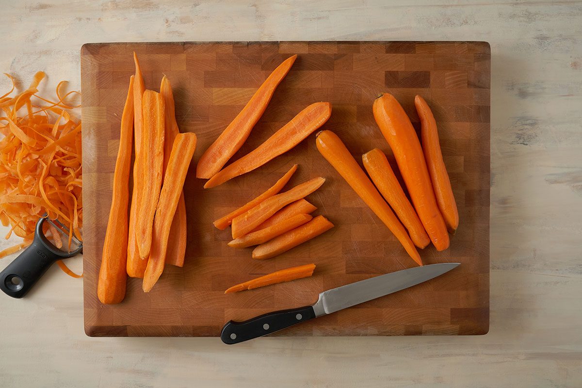 Overhead view of carrots being peeled and cut into cubes and halves for the Taste of Home Roasted Vegetables with Walnuts recipe.