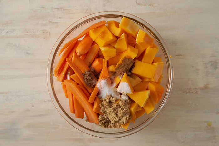 Overhead view of butternut squash and carrots in a large bowl with brown sugar, olive oil, cinnamon, nutmeg, and salt for the Taste of Home Roasted Vegetables with Walnuts recipe.