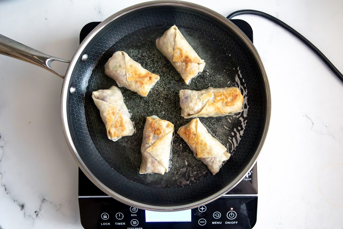 Overhead shot for Taste of Home Sausage Egg Rolls, frying egg rolls in a HexClad over Induction Cooktop.