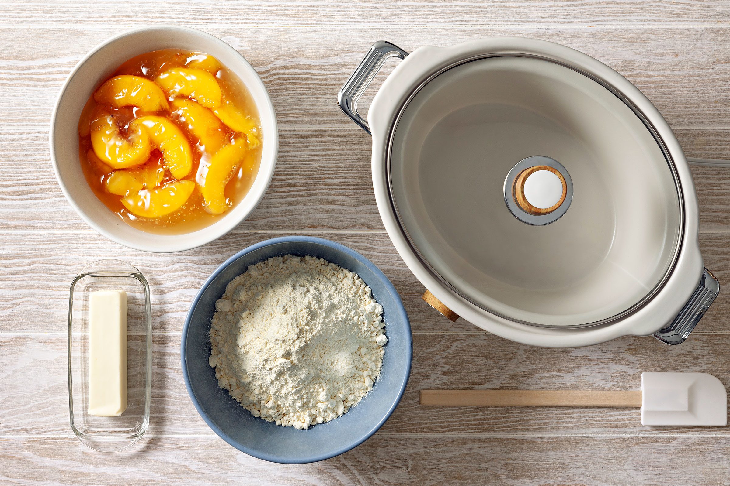 An empty cooker with bowls of canned peaches, butter and cake mix