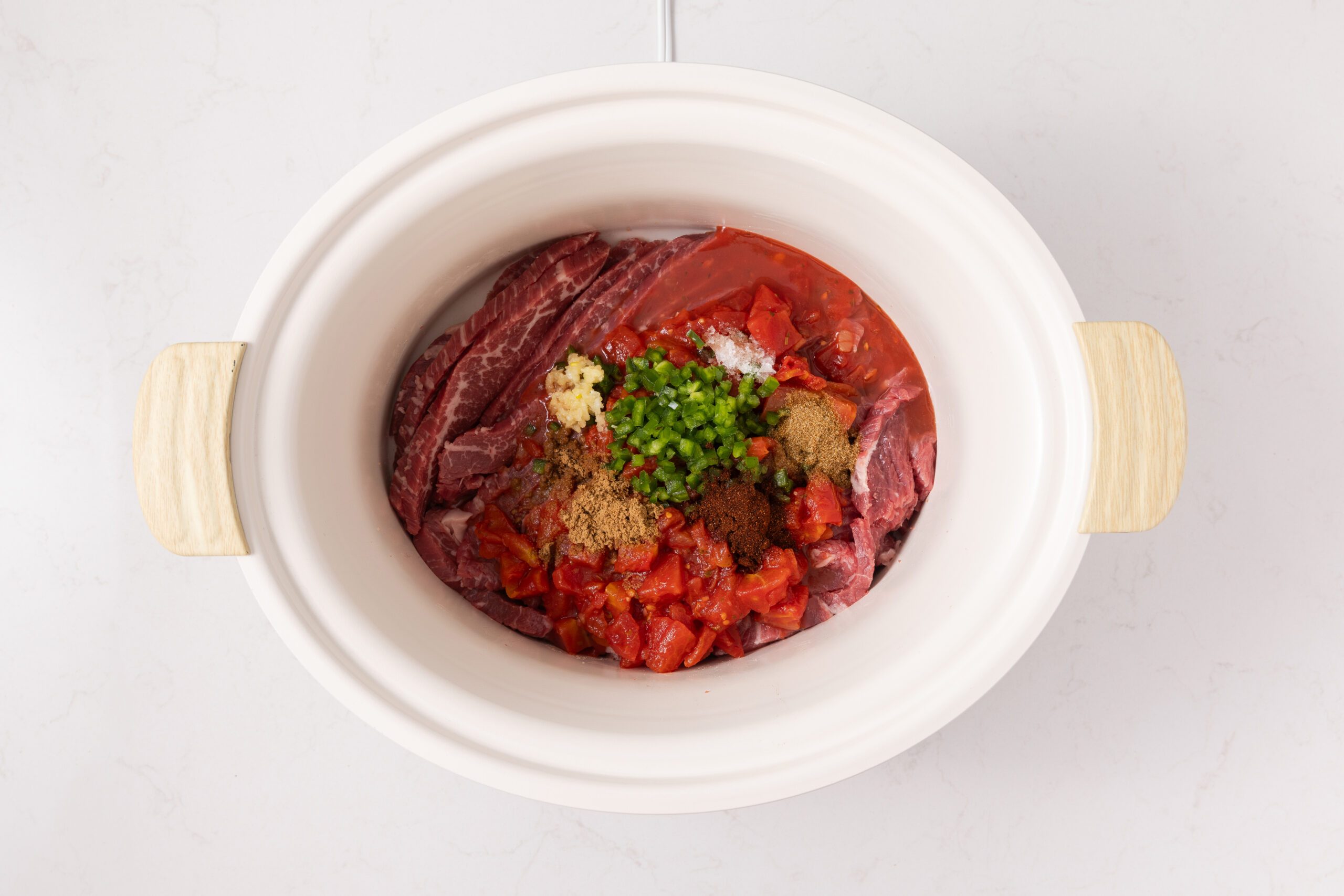 Beef flank steak sliced and placed in slow cooker with diced tomatoes, jalapeno pepper and seasonings.
