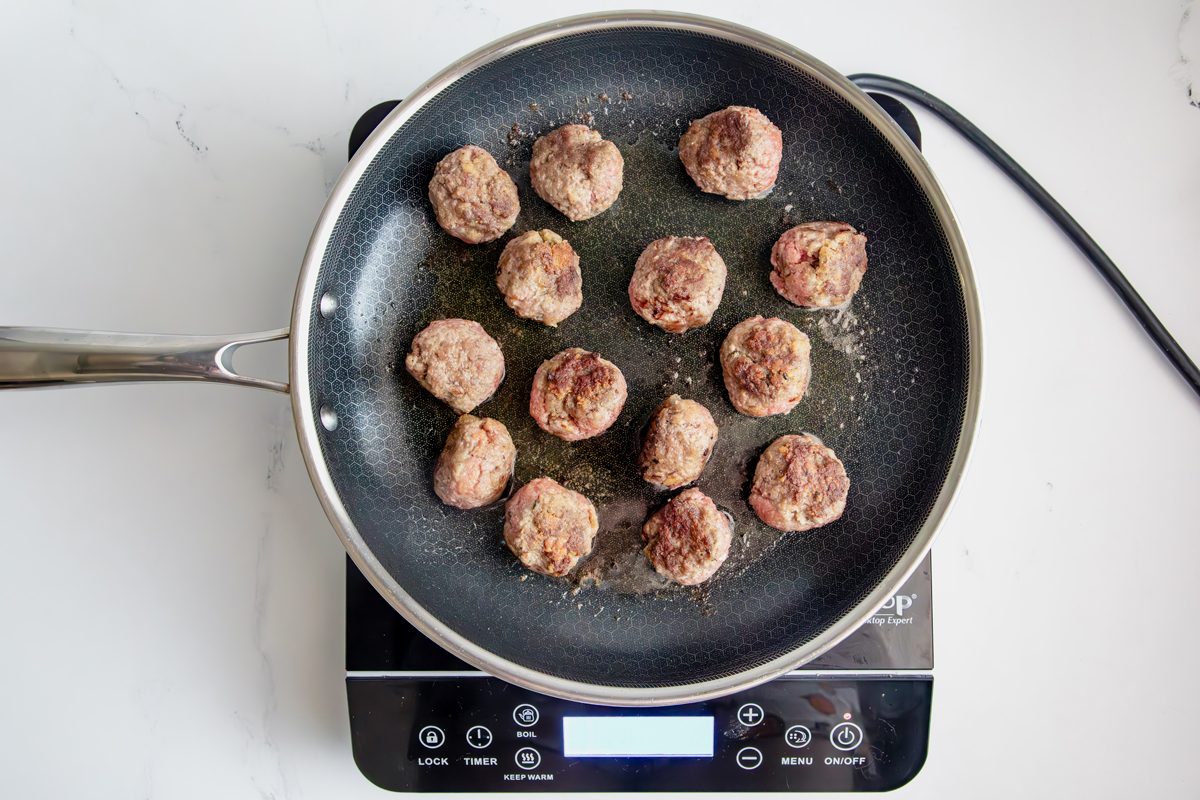 Overhead shot for Taste of Slow-Cooker Spaghetti and Meatballs, meatballs browning in a HexClad Pan over an induction cooktop.