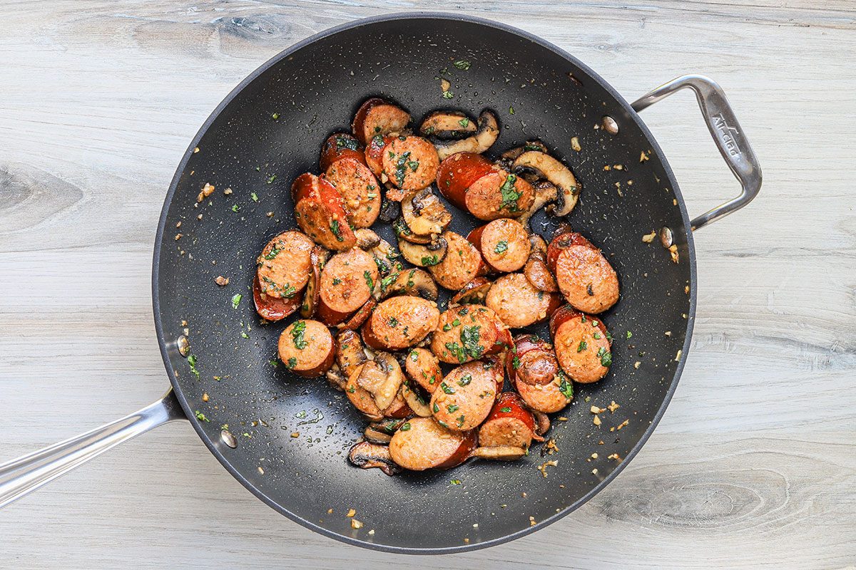 Smoked turkey kielbasa, mushrooms, garlic, and basil are browned in a skillet.