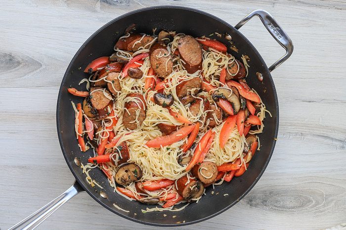Angel hair pasta and julienned plum tomatoes are added to the smoked sausage mixture in the skillet.