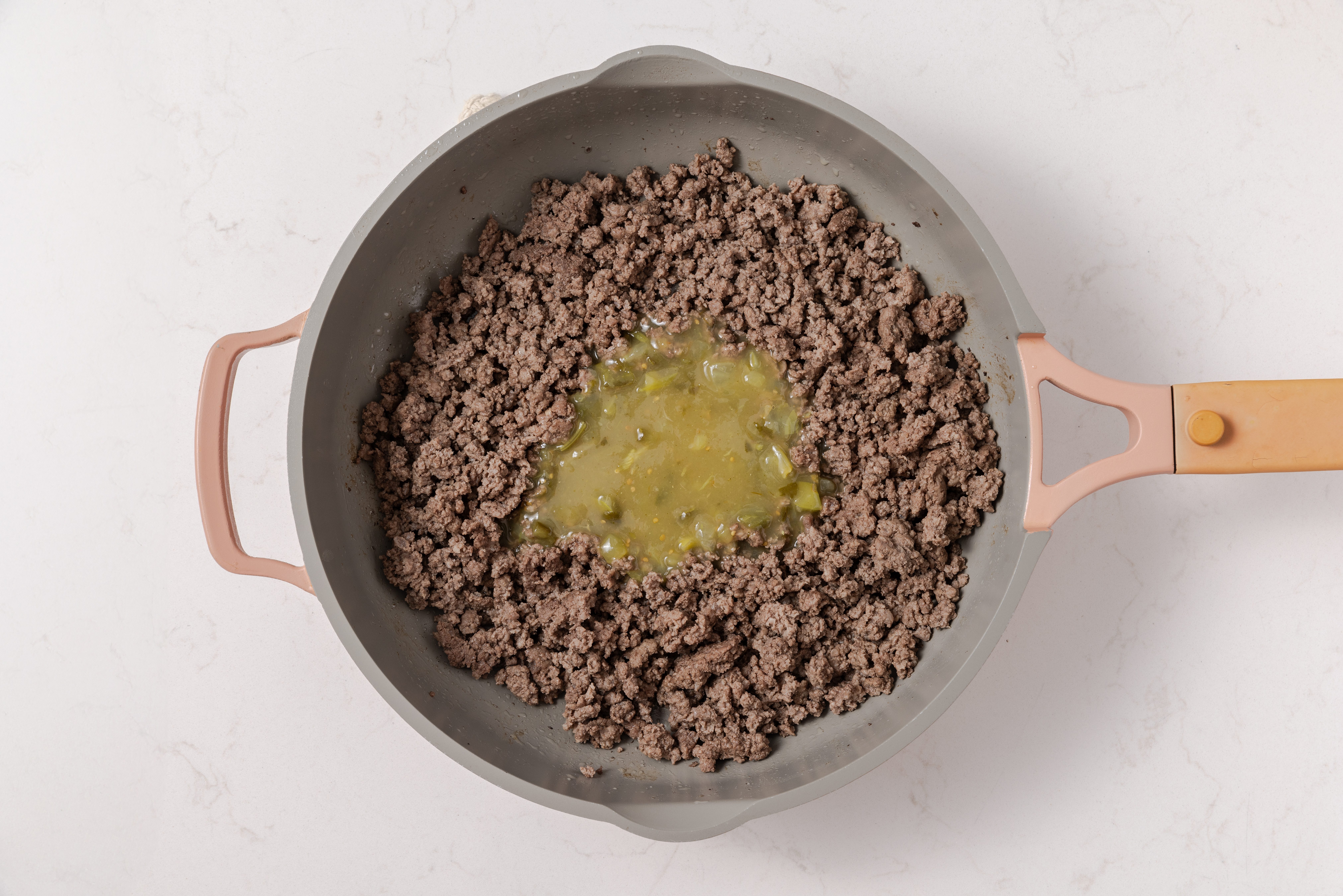 Beef cooked in skillet being combined with sauce mixture.