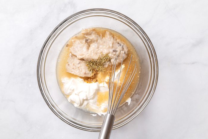 Cream of mushroom soup, sour cream, chicken broth, ground ginger. dried rosemary in a mixing bowl for step three of Smothered Pork Chops recipe for Taste of Home
