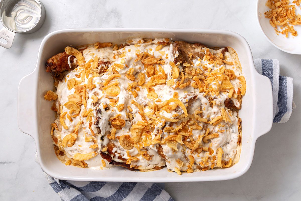 Baked pork chops and sauce topped with added sour cream and french fried onions in a baking dish for Smothered Pork Chops in Oven recioe for Taste of Home