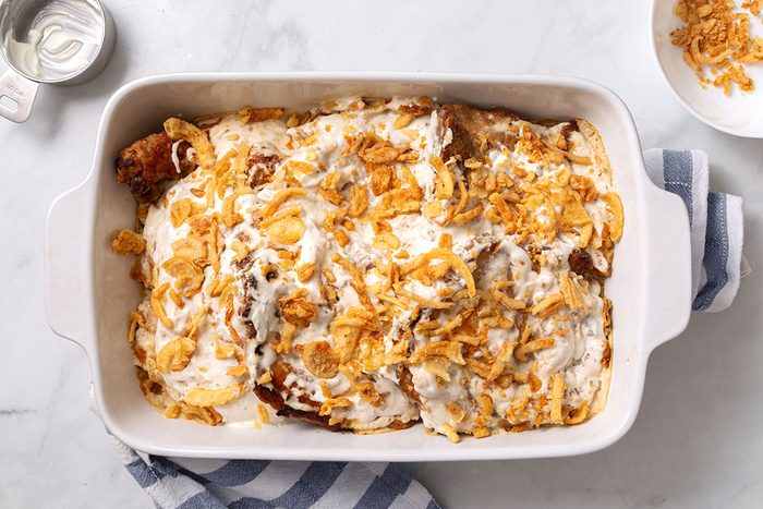Baked pork chops and sauce topped with added sour cream and french fried onions in a baking dish for Smothered Pork Chops in Oven recioe for Taste of Home