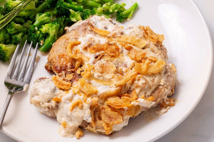 Smothered Pork Chops on a serving plate with a side of broccoli for Taste of Home