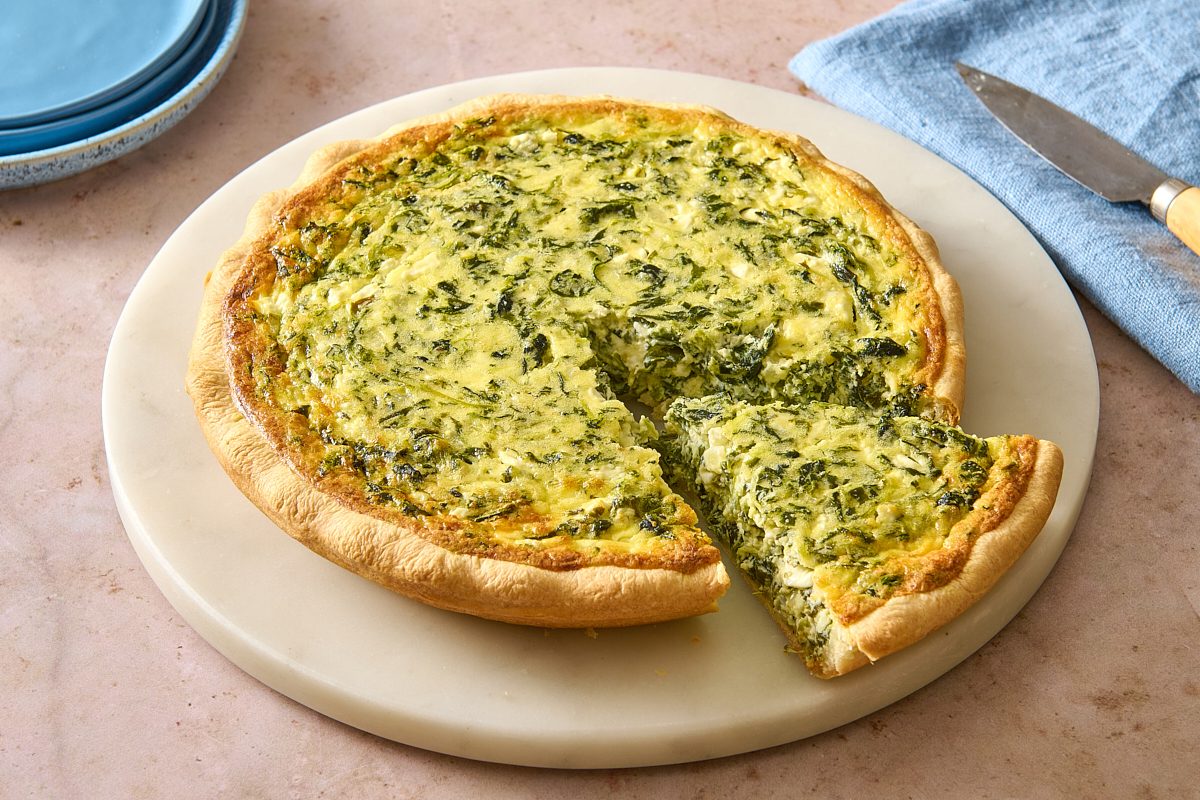 Angled shot of spinach pie on a platter with a slice partially removed