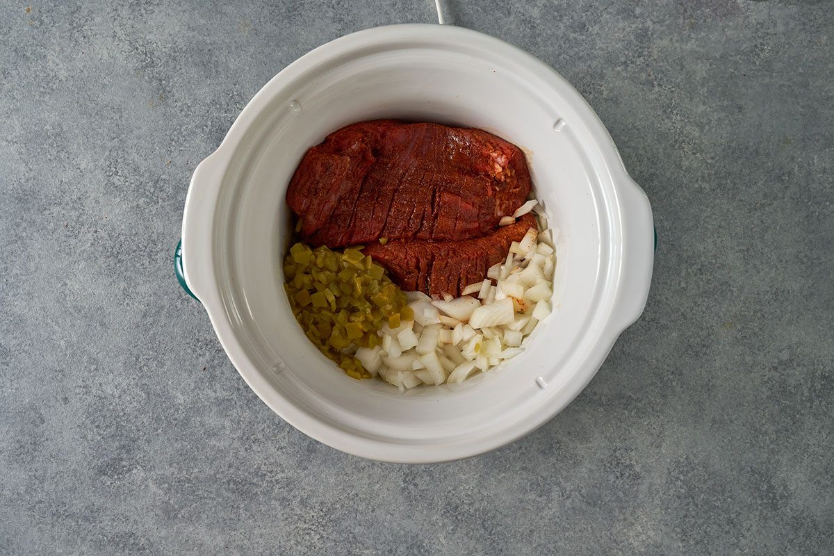 Place the seasoned steaks in a slow cooker coated with cooking spray. Top with onion, chiles, and vinegar, and cook on low until tender for eight to nine hours.