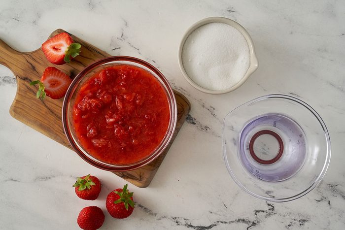A shot of the key ingredients for the Strawberry Syrup recipe, including sugar, water, and fresh strawberries, by Taste of Home.