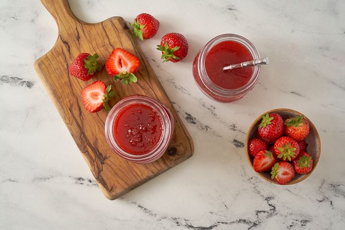 An overhead view of the Strawberry Syrup, rich and vibrant, served in a jar with fresh strawberries on the side, by Taste of Home.