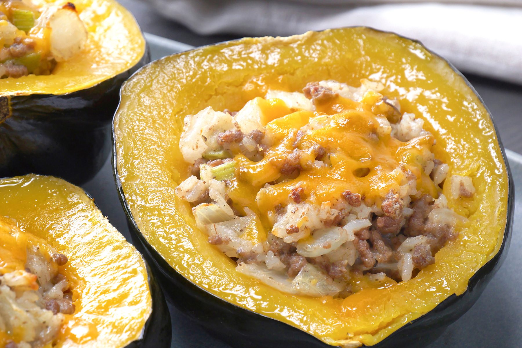 a close-up of stuffed acorn squash halves, The squash shells are a vibrant orange color, while the filling is a mixture of ground meat (likely beef or sausage), rice, vegetables, and melted cheese, The filling is a golden brown color and is topped with a layer of shredded cheddar cheese;