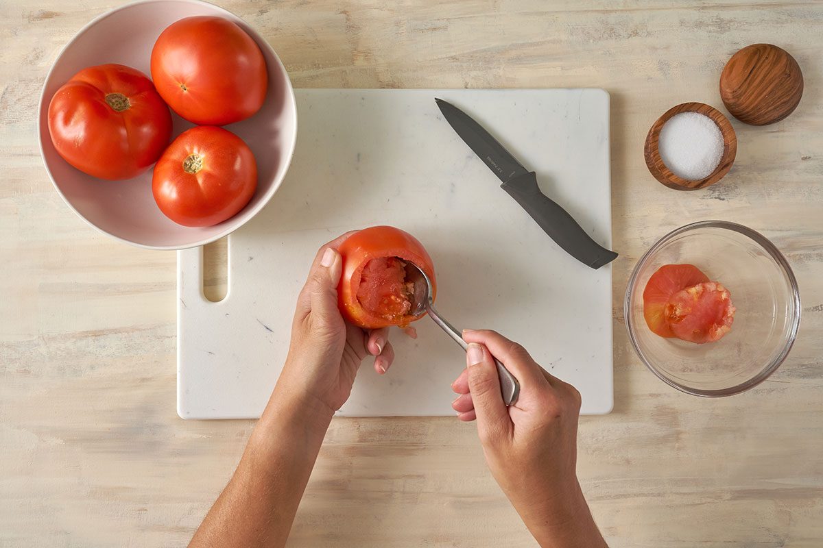 Tomatoes being prepared by scooping out the pulp and leaving a 1/2-inch shell for the Stuffed Tomatoes with Rice recipe, by Taste of Home.